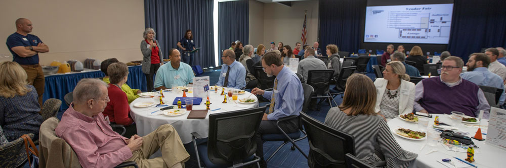 Several tables of community members listen to a presentation given during UVA's Apprenticeship Summit