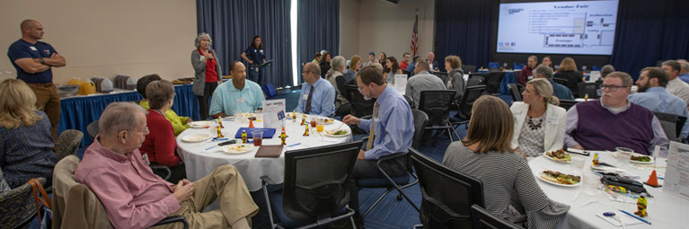 Several tables of community members listen to a presentation given during UVA's Apprenticeship Summit