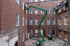 An FM employee in a cherrypicker works on the exterior brick of Alderman Library