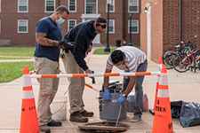 Facilities Management workers draw wastewater from a manhole near a UVA dorm