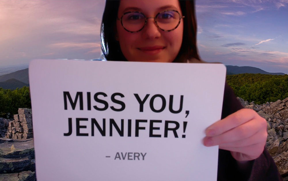 Avery Wagner holding up a sign reading 'Miss you, Jennifer!'
