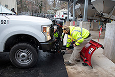 Two FM employees secure a snowplow to a pickup truck