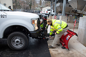 Two FM employees secure a snowplow to a pickup truck