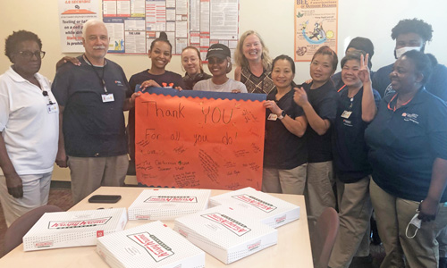 The Housing Custodial team hold up a thank-you sign while standing around a table of Krispy Kreme donuts