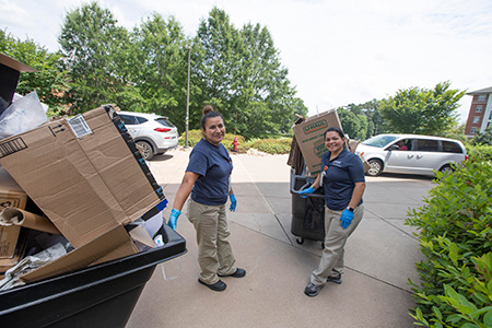 Two Facilities Management workers rolling large plastic bins full of cardboard