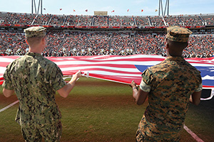 Military veterans holding a large American flag on a football field