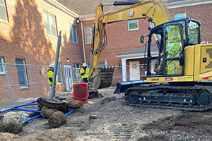 A backhoe excavating soil and two Utilities employees nearby