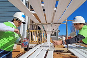 Two women voluneers paint long wooden slats