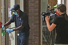 A Facilities employee sanitizing a door while being filmed by a cameraperson