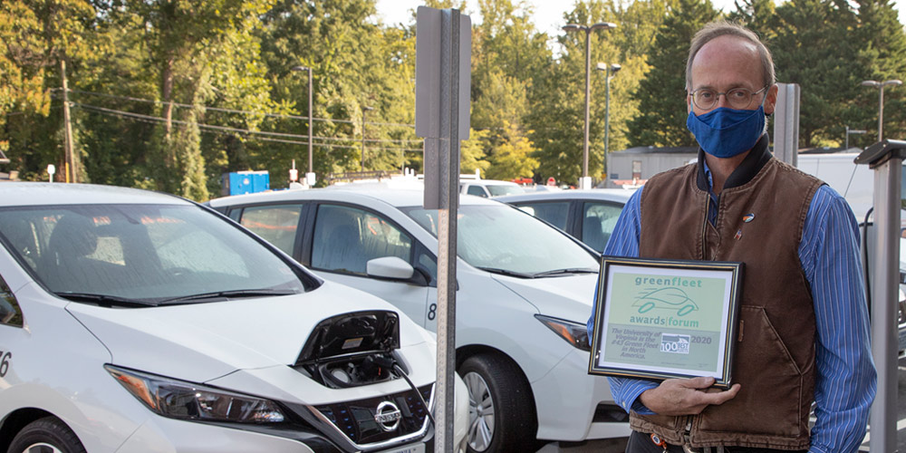 Transportation Operations and Fleet Manager Mike Duffy holds Green Fleet award, standing by a recharging Nissan Leaf