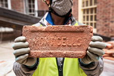 An FM employee in PPE holds up a brick stamped with the word Monticello
