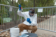 An FM employee in personal protective equipment takes a sample of wastewater