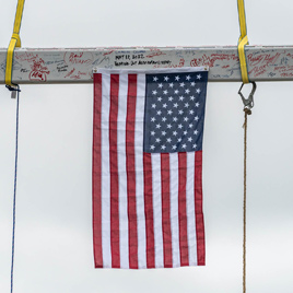 A steel beam suspended by a crane, covered in signatures and hanging an American flag