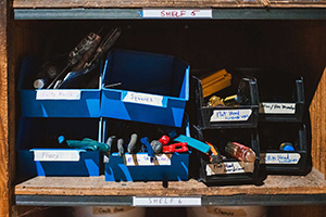 A shelf with labeled small plastic storage bins holding various hand tools