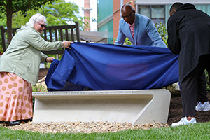 A memorial bench being unveiled by two FM employees and an associate professor