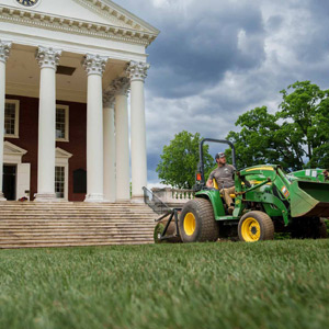 A man rides a compact tractor in front of The Rotunda