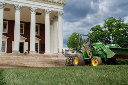 A man rides a compact tractor in front of The Rotunda
